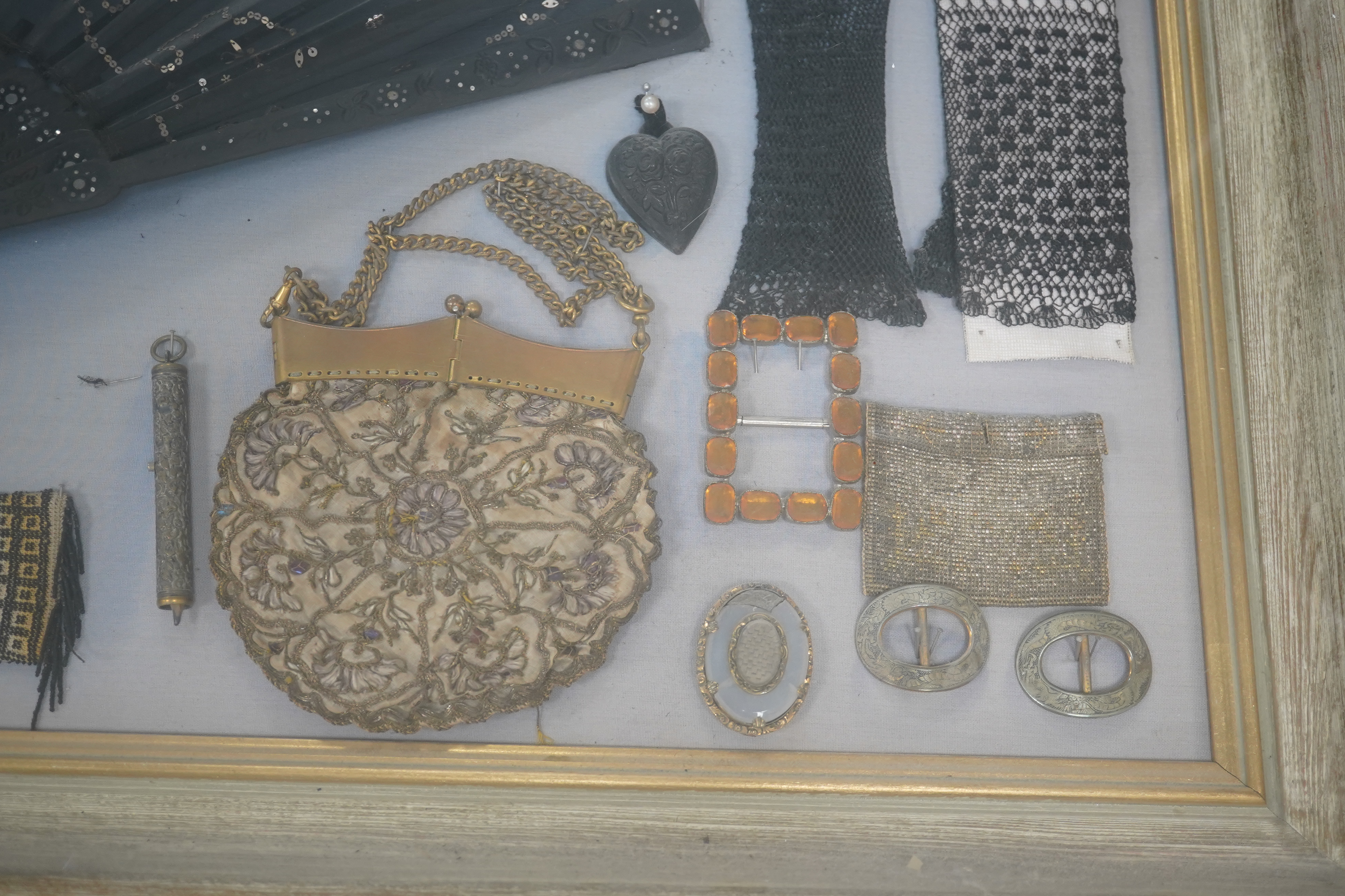 A framed display montage of late 18th and 19th century decorative ladies sequin and lace fans, beadwork reticules, cut steel misers purses, hat pins, earrings, brooches, shoe buckles and crochet mittens.100cm x 70cm. Con